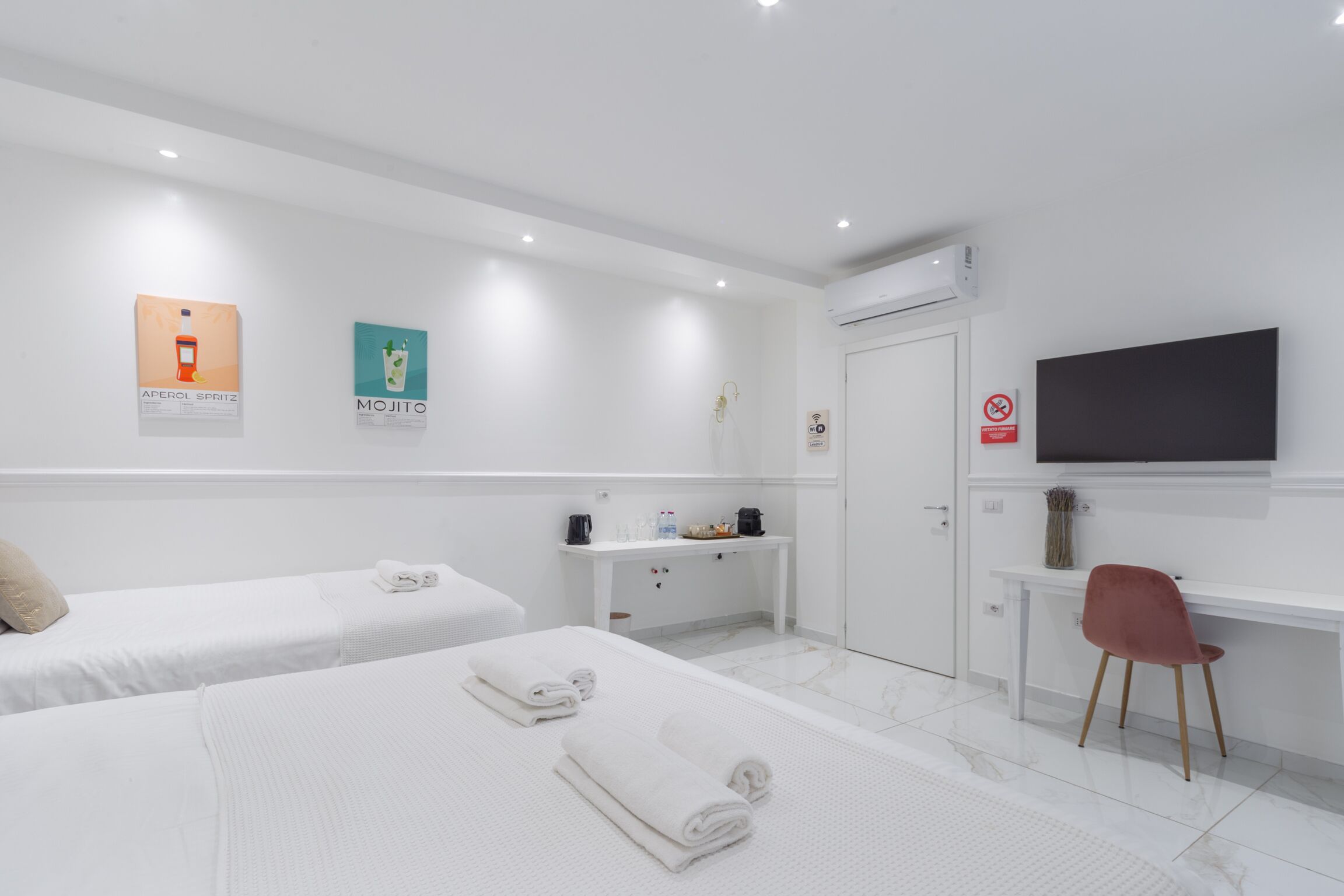 A hotel room with two beds, a desk, a TV, and a small seating area.