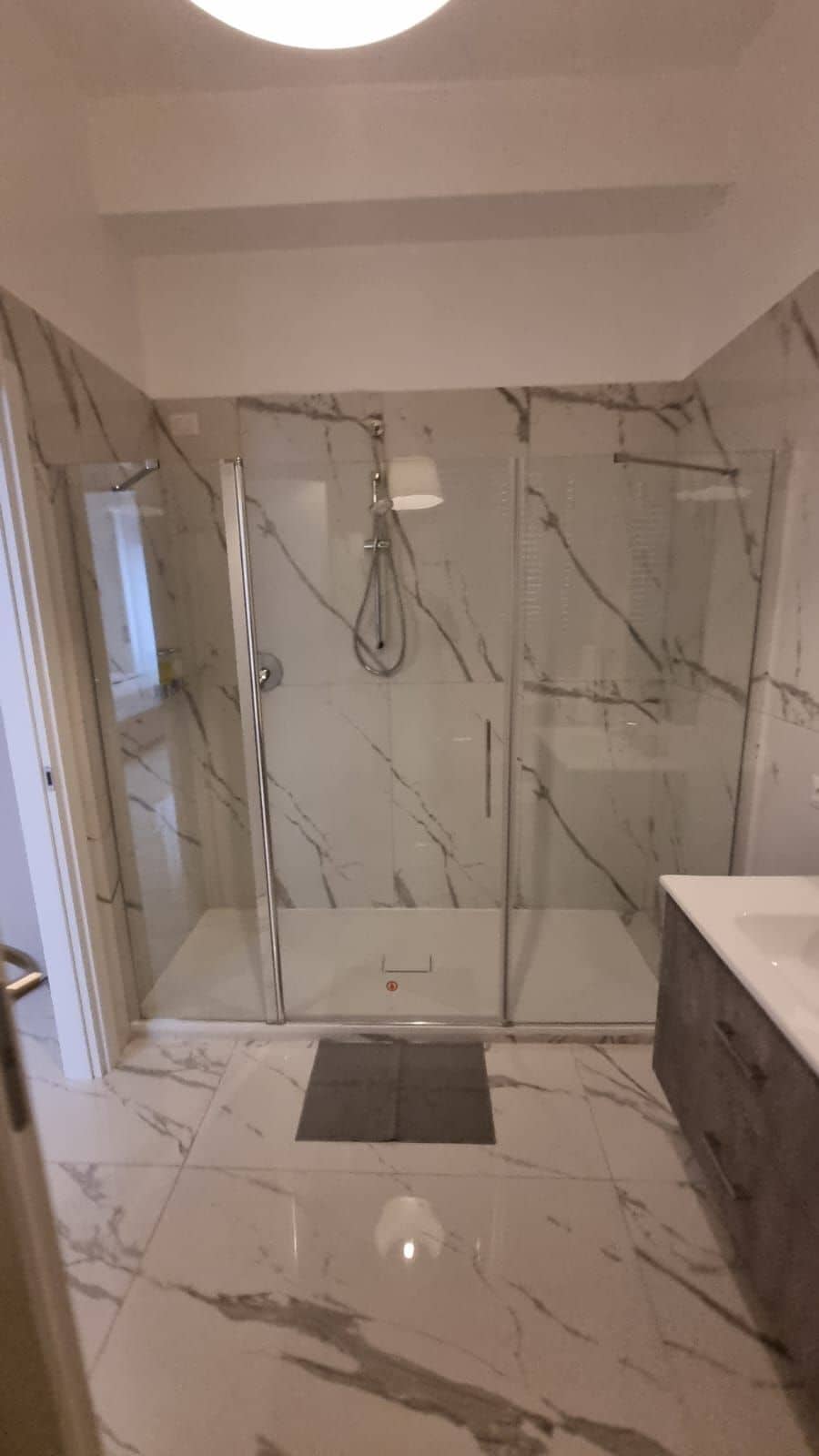 Un baño con ducha envuelta en cristal, paredes de mármol y un lavamanos.