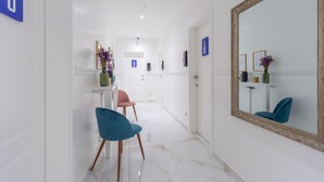 A hallway with a blue chair, a pink chair, a mirror, and a door with a sign. - Leia Hospitality (Milan)