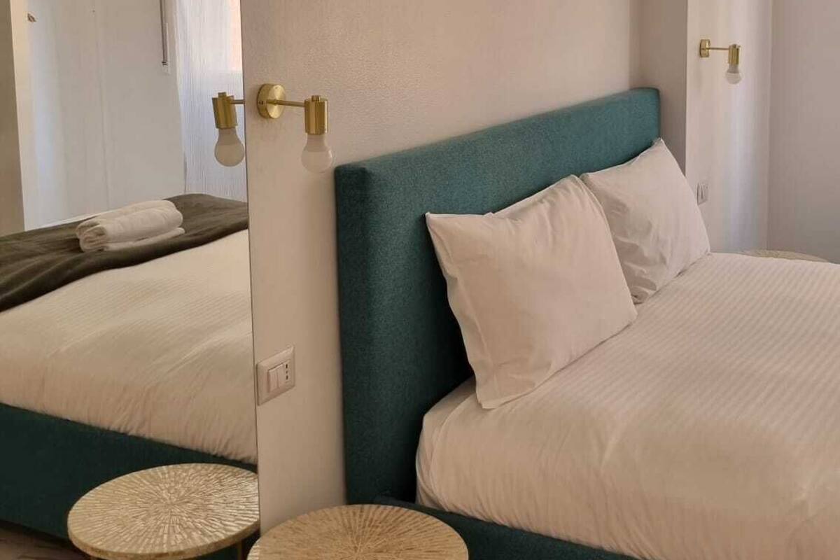 A modern bedroom with a teal headboard, a large mirror, and two round stools.