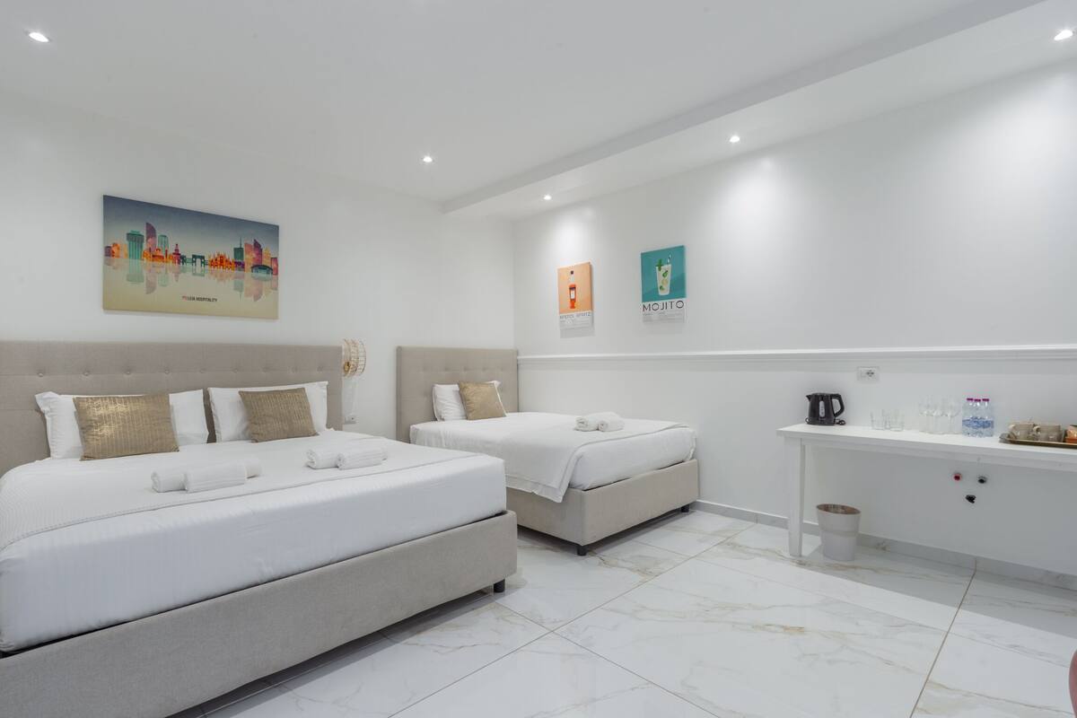 A hotel room with two beds, a minibar, and a cityscape painting on the wall.