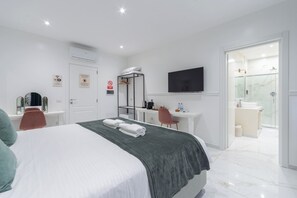 A modern hotel room with a bed, a desk, a TV, and a bathroom visible through an open door.