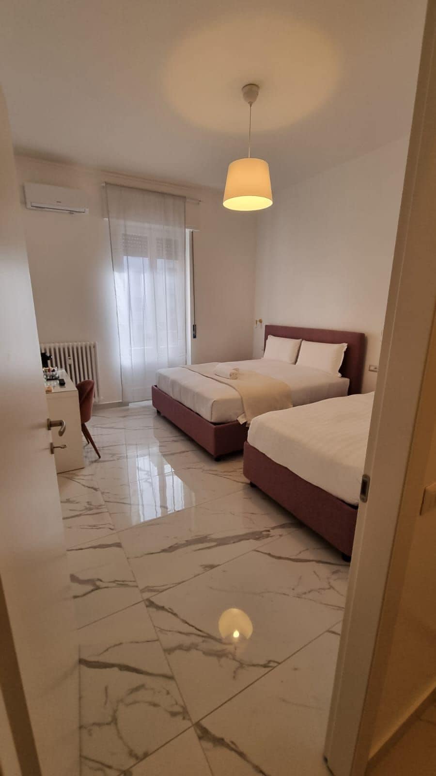 A hotel room with two beds, a desk, and a radiator.