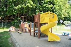 A playground with a yellow spiral slide and wooden climbing structures. - Adirondack Retreat Inn & Suites - TOWNHOUSE RENTAL HOUSE (Lake George)