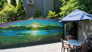 Un patio con un mural de un paisaje, mobiliario exterior y una zona con sombra.