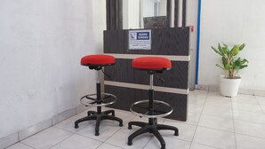 Deux tabourets rouges rembourrés, dotés d’une structure et de roulettes en métal, sont placés devant un comptoir en bois foncé, au-dessus duquel est accrochée une enseigne.