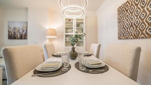 Een eetruimte met een tafel voor vier personen, een vaas met een plant en een decoratieve wandversiering.