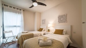 Een hotelkamer met twee bedden, een plafondventilator, een stoel en decoratieve wandkunst.