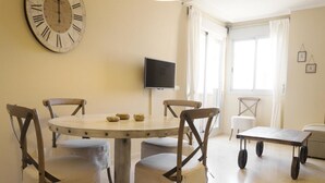 Un coin repas comprenant une table ronde, quatre chaises, un téléviseur et une fenêtre avec des rideaux.