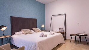 A modern hotel room with a large bed, two bedside lamps, a small round table, a chair, and a large mirror.