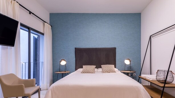 A bedroom with a large bed, two bedside tables with lamps, a chair, and a TV mounted on the wall.