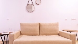 A beige sofa with two cushions in a minimalist room with a round table and a glass on the left.