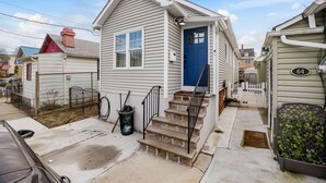 A single-story house with a blue front door, a small front porch, and a visible number '64' on the side. - Dog-friendly Single-Family Home w Free Parking, Washer, Dryer in NYC "Nantucket" (The Bronx)