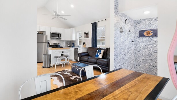 A compact living space with a kitchenette, a dining area with a wooden table, a black leather sofa, and a patterned wall. - Dog-friendly Single-Family Home w Free Parking, Washer, Dryer in NYC "Nantucket" (The Bronx)