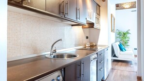 Une cuisine moderne dotée d’un lave-linge et d’un sèche-linge int égrés, d’un plafond en bois et offrant une vue sur un espace de vie avec un canapé.