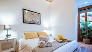 Ein Hotelzimmer mit einem Bett, zwei Nachttischlampen, einer gerahmten Karte an der Wand, einem Tablett mit Frühstücksgegenständen und einer Topfpflanze.