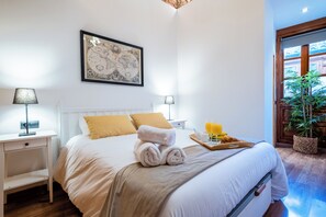 Ein Hotelzimmer mit einem Bett, zwei Nachttischlampen, einer gerahmten Karte an der Wand, einem Tablett mit Frühstücksgegenständen und einer Topfpflanze.