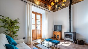 Un salon comprenant un canapé, une table basse en verre, un téléviseur, un meuble en bois et un poêle à bois.