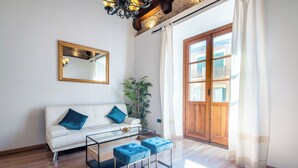 Ein modernes Wohnzimmer mit einem weißen Sofa, blauen Kissen, einem Glastisch und einer Holztür, die nach draußen führt.