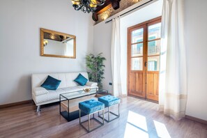 Ein modernes Wohnzimmer mit einem weißen Sofa, blauen Kissen, einem Glastisch und einer Holztür, die nach draußen führt.