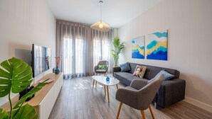 Un salon moderne avec un canapé, des fauteuils, une table basse, un téléviseur et des œuvres d’art accrochées au mur.