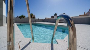 Une piscine à l’eau d’un bleu cristallin, entourée d’une terrasse carrelée et dotée d’échelles métalliques.