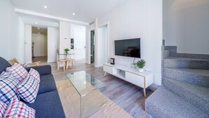 A modern living room with a sofa, a glass coffee table, a TV, and a staircase.
