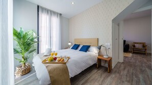 A modern hotel room with a large bed, a bedside table with a lamp, a tray with fruits and juice, and a potted plant.