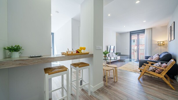 A modern kitchen with a bar area, wooden flooring, and a seating area with a sofa and chairs.
