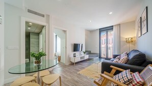 A modern living room with a glass dining table, wooden chairs, a sofa, and a TV.