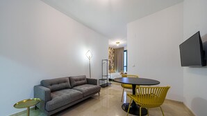 Ein modernes Hotelzimmer mit einer Couch, einem Esstisch mit Stühlen, einem an der Wand befestigten Fernseher und einer Stehlampe.