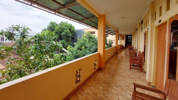 A corridor with a tiled floor, wooden benches, and a covered balcony with a view of greenery and buildings. - Hotel O Rasya Homestay Near SD Negeri 6 Mataram (Mataram)