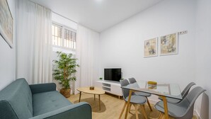 Un salon moderne avec un canapé, une table à manger, des chaises, un téléviseur et une plante en pot.