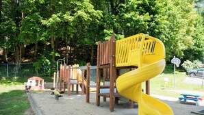 A playground with a yellow spiral slide, wooden climbing structures, and a fenced area. - Adirondack Retreat Inn & Suites - Superior Rental House (Lake George)