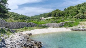 A coastal landscape with a stone wall, a clear beach, and a house on a hill. - Villa Blue Bay with private pool (Selca)