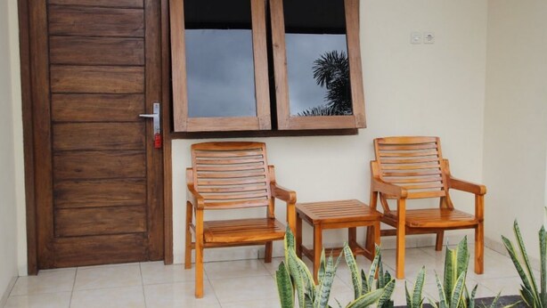 Una puerta de madera con el número 15, dos sillas de madera y una pequeña mesa frente a una pared con dos ventanas.