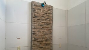 Una ducha con diseño de pared de piedra, un grifo y un dispensador de jabón.