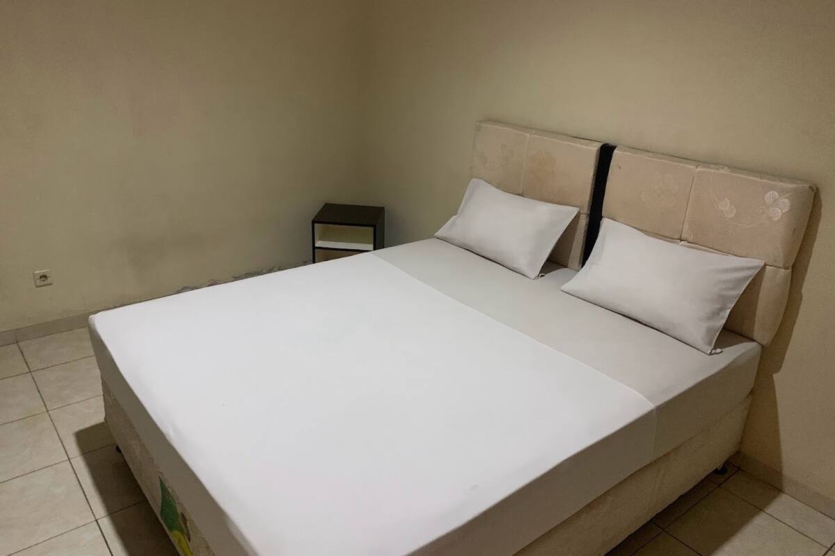 Una cama individual con cabecera, mesita de noche y toma de corriente.
