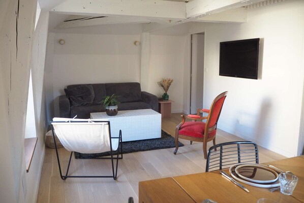 Ein Wohnzimmer mit Sofa, Couchtisch, Esstisch mit Stühlen und einem an der Wand befestigten Fernseher.