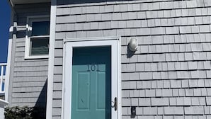 Une maison avec une porte de couleur turquoise portant le numéro « 101 » et un porche blanc.