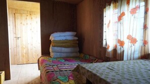Une pièce avec une porte en bois, un lit recouvert d’une courtepointe aux couleurs vives, une pile d’oreillers et une fenêtre ornée de rideaux à motifs floraux.