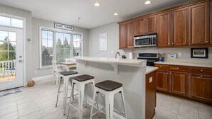 A kitchen with wooden cabinets, a white countertop, and three bar stools. - DOG FRIENDLY-POOL/TENNIS COMMTY CLOSE TO REHO BEACH & BOARDS -37287 Trent Ct. (Rehoboth Beach)