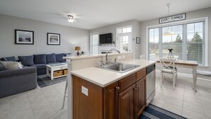 A modern living room with a grey sofa, a white coffee table, and a kitchen area with a sink, stove, and dining table. - DOG FRIENDLY-POOL/TENNIS COMMTY CLOSE TO REHO BEACH & BOARDS -37287 Trent Ct. (Rehoboth Beach)