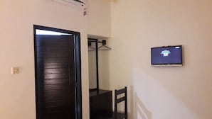 Een kamer met een deur, een stoel, een aan de muur bevestigde televisie en een kapstok.
