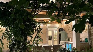 Un espacio exterior bien iluminado con un muro de piedra, una pérgola de madera y diversas plantas y flores.