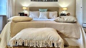 Un dormitorio con cama, mesitas de noche, lámpara, un cuadro y un banco de madera.