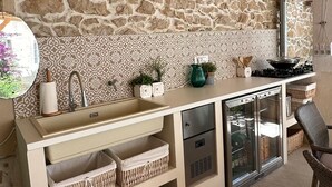 Una cocina con pared de piedra, pileta, estufa y refrigerador.
