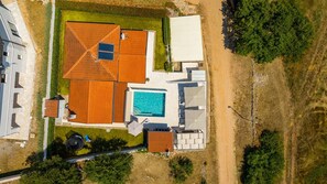 Eine Luftaufnahme eines Grundstücks mit Schwimmbad, überdachter Terrasse und umzäunter Garten.