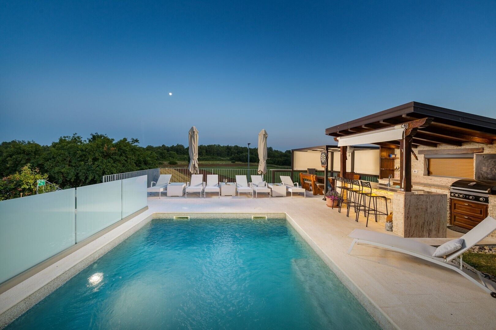 Un espace piscine aménagé sur le toit, avec des chaises longues, un barbecue et une vue sur le ciel nocturne.