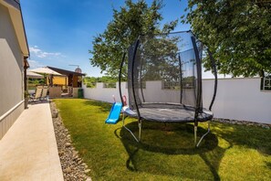 A backyard with a trampoline, a slide, and a patio area with outdoor furniture. - Gloria Vita - villa with private pool and indoor jacuzzi (Nova Vas)